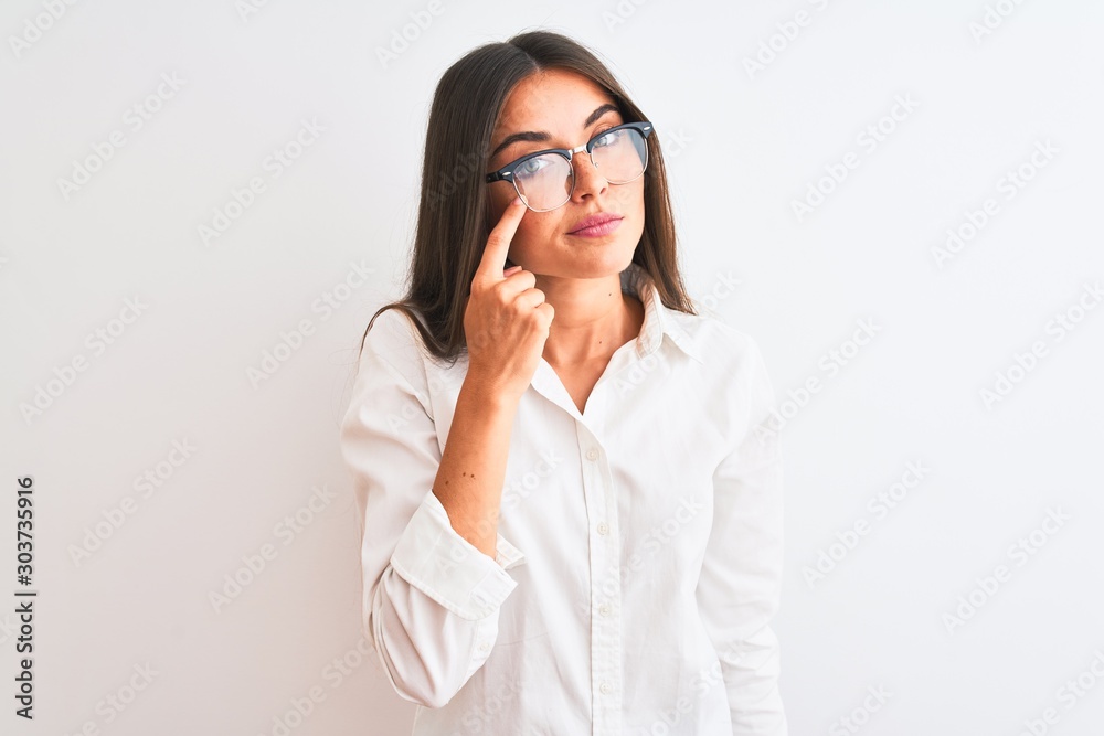 Young beautiful businesswoman wearing glasses standing over isolated white background Pointing to the eye watching you gesture, suspicious expression