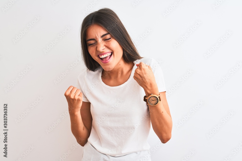 Young beautiful woman wearing casual t-shirt standing over isolated white background very happy and excited doing winner gesture with arms raised, smiling and screaming for success. Young beautiful woman wearing casual t-shirt standing over isolated white background very happy and excited doing winner gesture with arms raised, smiling and screaming for success.