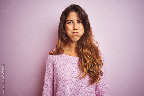 Young beautiful woman wearing sweater standing over pink isolated background puffing cheeks with funny face. Mouth inflated with air, crazy expression.