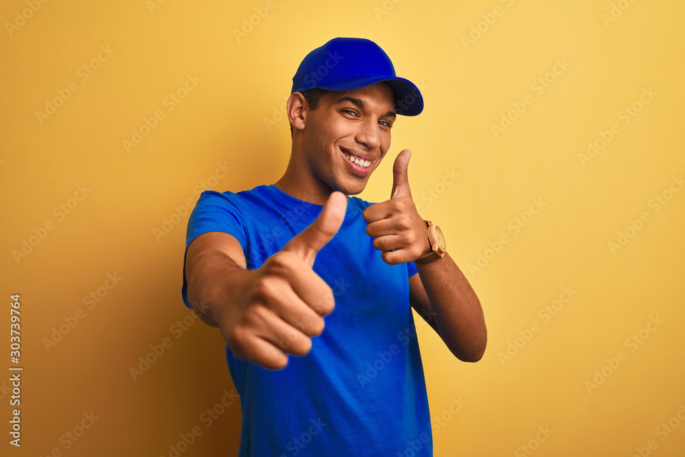 Young handsome arab delivery man standing over isolated yellow background approving doing positive gesture with hand, thumbs up smiling and happy for success. Winner gesture. Young handsome arab delivery man standing over isolated yellow background approving doing positive gesture with hand, thumbs up smiling and happy for success. Winner gesture.