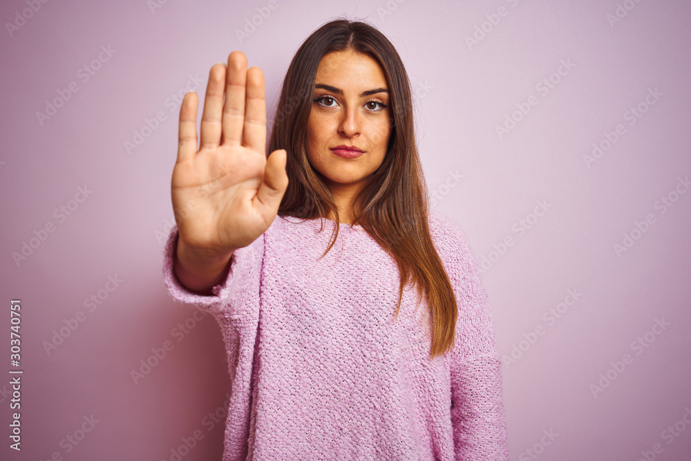 Young beautiful woman wearing casual sweater standing over isolated pink background doing stop sing with palm of the hand. Warning expression with negative and serious gesture on the face. Young beautiful woman wearing casual sweater standing over isolated pink background doing stop sing with palm of the hand. Warning expression with negative and serious gesture on the face.