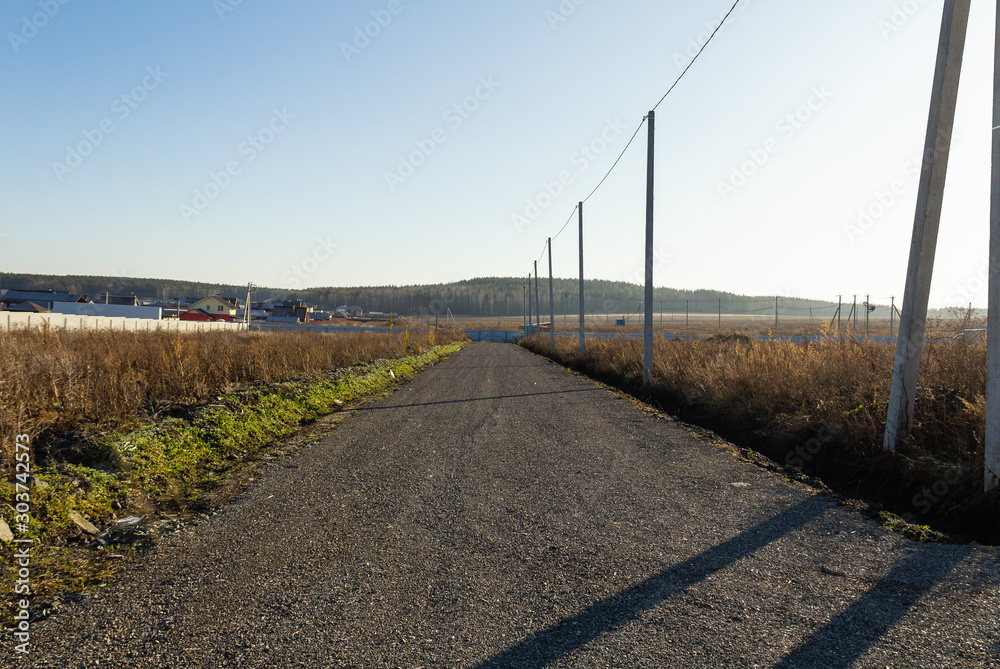 Dirt road with electric poles in a cottage village. Autumn, sunny