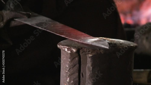 A daylight extreme closeup shot of a red, hot metal fresh from the fire being hammered flat on top of a round, thick iron block by a local blacksmith. 