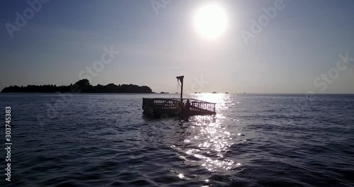 Young couple sitting on platform floating over calm tranquil lagoon near tropical island bay during sunset moments in Thailand