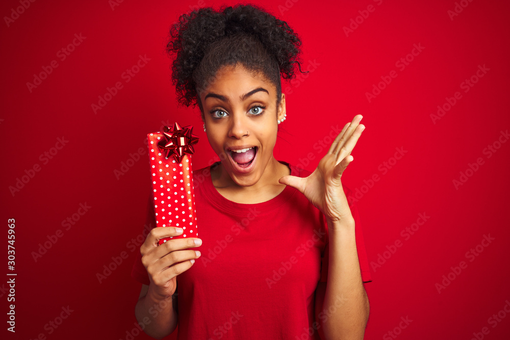 Young african american woman holding valentine gift over isolated red background very happy and excited, winner expression celebrating victory screaming with big smile and raised hands Young african american woman holding valentine gift over isolated red background very happy and excited, winner expression celebrating victory screaming with big smile and raised hands
