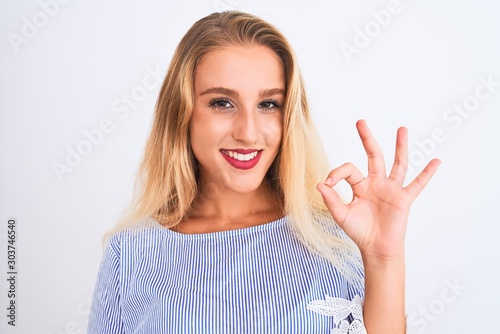 Young beautiful woman wearing elegant blue t-shirt standing over isolated white background doing ok sign with fingers, excellent symbol