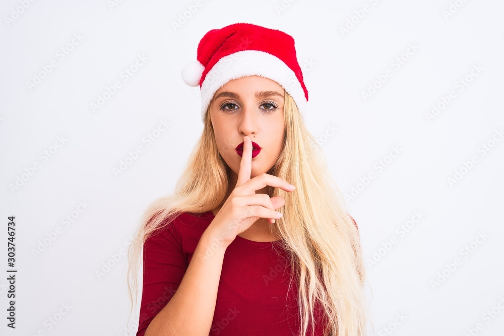 Young beautiful woman wearing Christmas Santa hat over isolated white background asking to be quiet with finger on lips. Silence and secret concept. Young beautiful woman wearing Christmas Santa hat over isolated white background asking to be quiet with finger on lips. Silence and secret concept.