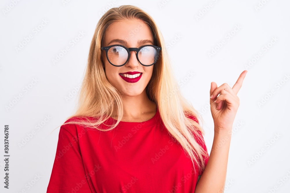 Young beautiful woman wearing red t-shirt and glasses standing over isolated white background with a big smile on face, pointing with hand and finger to the side looking at the camera.