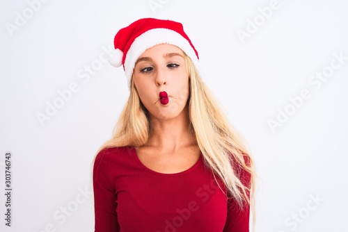 Young beautiful woman wearing Christmas Santa hat over isolated white background making fish face with lips  crazy and comical gesture. Funny expression.