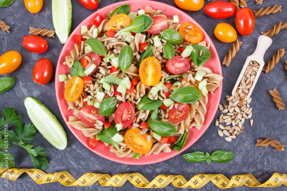 Tape measure and salad with wholegrain pasta and vegetables as healthy meal containing vitamins and minerals