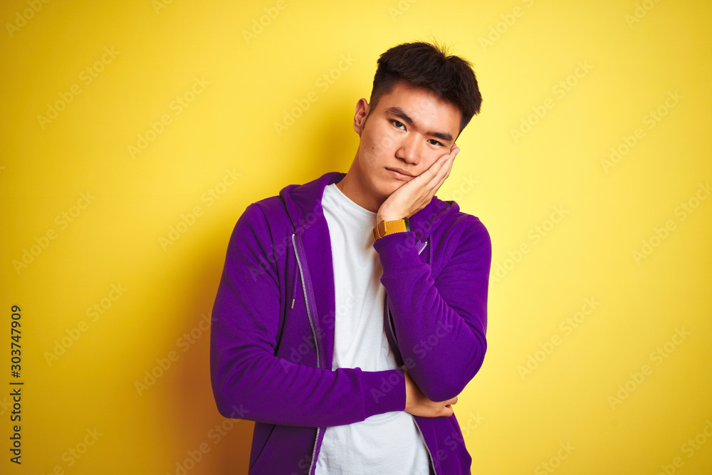 Φωτογραφία Young asian chinese man wearing purple sweatshirt standing over isolated yellow background thinking looking tired and bored with depression problems with crossed arms
