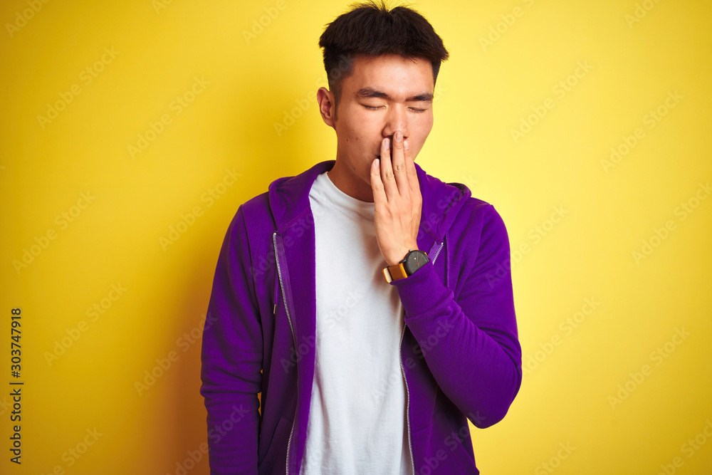Φωτογραφία Young asian chinese man wearing purple sweatshirt standing over isolated yellow background bored yawning tired covering mouth with hand