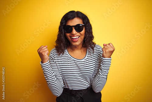 Transsexual transgender woman wearing sunglasses over isolated yellow background celebrating surprised and amazed for success with arms raised and open eyes. Winner concept. © Krakenimages.com