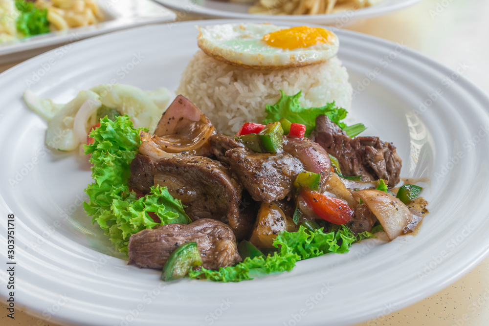 Asian Chinese Stir-fried spicy pepper beef with lettuce, jasmine white rice, pickled vegetables and sunny-side up fried egg