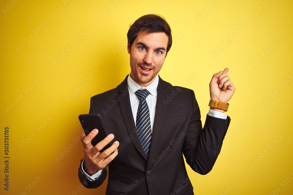 Young handsome businessman using smartphone standing over isolated yellow background very happy pointing with hand and finger to the side Young handsome businessman using smartphone standing over isolated yellow background very happy pointing with hand and finger to the side