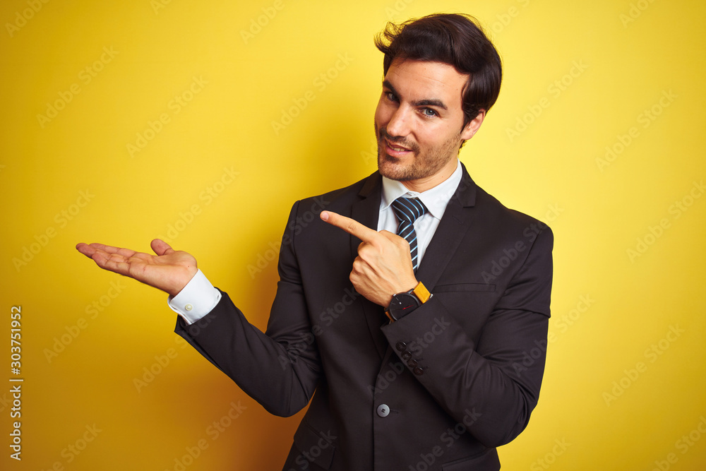 Φωτογραφία Young handsome businessman wearing suit and tie standing over isolated yellow background amazed and smiling to the camera while presenting with hand and pointing with finger