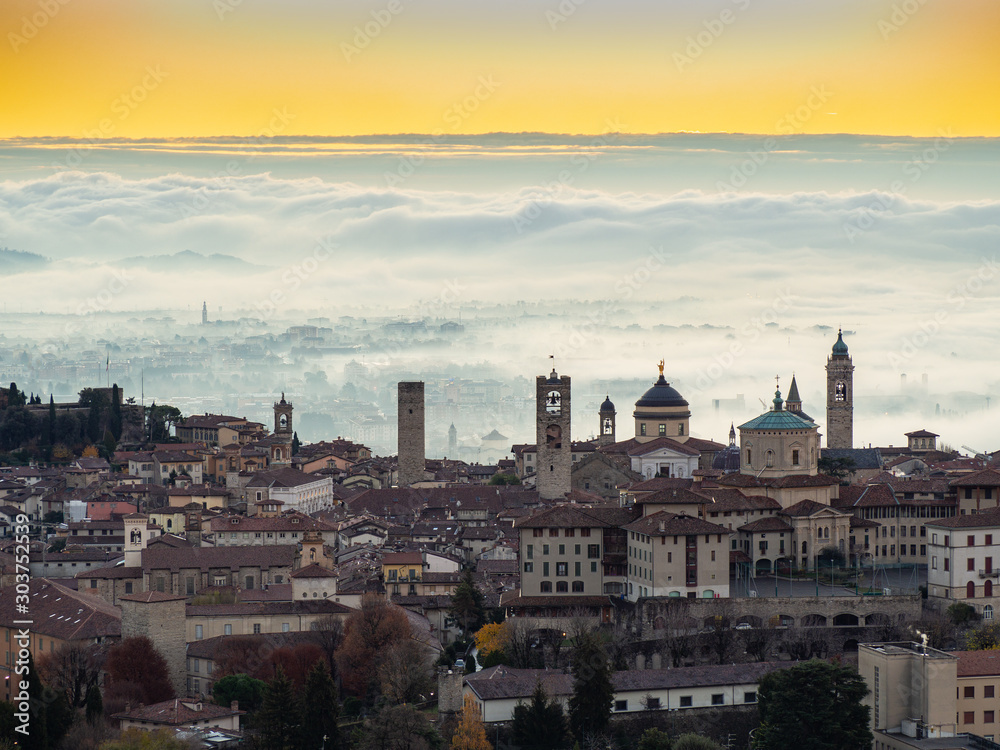 Bergamo, Italy. Amazing landscape of the town covered by the fog arising from the plain. Fall season. Morning. Sunrise time