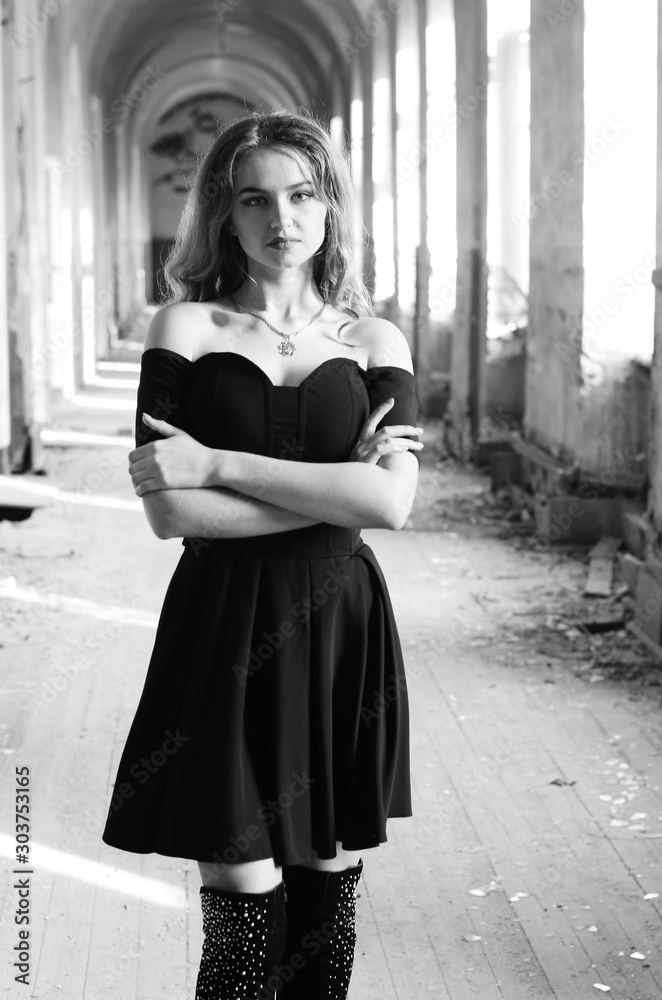 Young beautiful short hair blonde woman in black climbing the stairs, black  and white photo. Side view of elegant romantic mysterious lady with movie  star look in interior with bricks walls Stock
