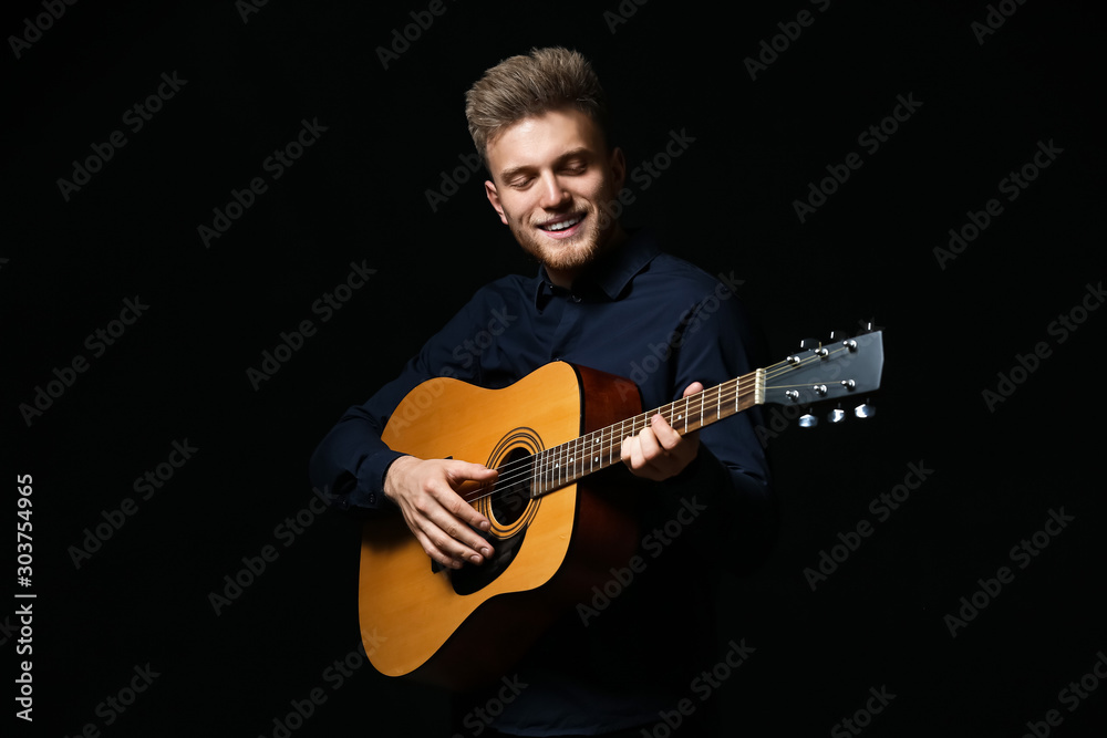 Handsome man playing guitar on dark background