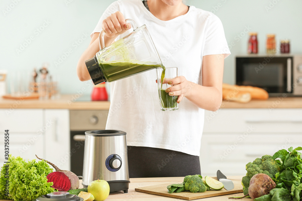 Woman pouring healthy smoothie into glass in kitchen Woman pouring healthy smoothie into glass in kitchen