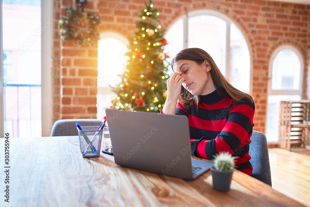 Φωτογραφία Beautiful woman sitting at the table working with laptop at home around christmas tree tired rubbing nose and eyes feeling fatigue and headache