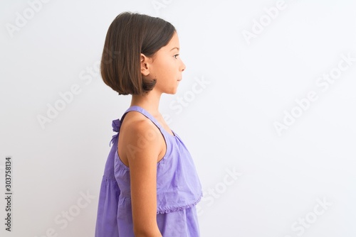 Young beautiful child girl wearing purple casual dress standing over isolated white background looking to side, relax profile pose with natural face with confident smile.