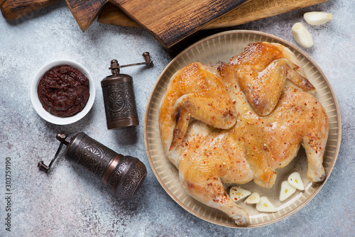 Round plate with pan fried chicken tapaka over beige stone background, flatlay, horizontal shot photo