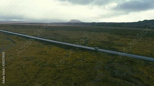 4WD off-road jeep with turned on headlights is driving up the green hill by the unpaved dirt gravel road. The cloudy sky and blue sea on the background at the dusk. Sprengisandur, Iceland. oktober