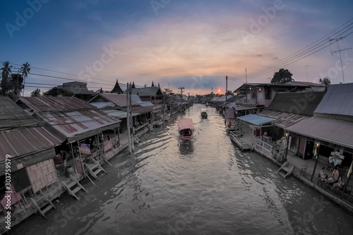 view evening of long-tail boats running in Amphawa Canal around with wooden houses and cloudy sky background, sunset at Amphawa Floating Market, Samut Songkhram, Thailand.