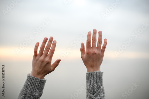 beautiful young hands in a warm woolen sweater raised up to the sky on a sunset background