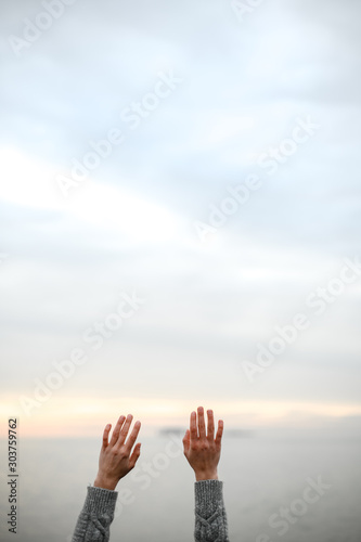beautiful young hands in a warm woolen sweater raised up to the sky on a sunset background