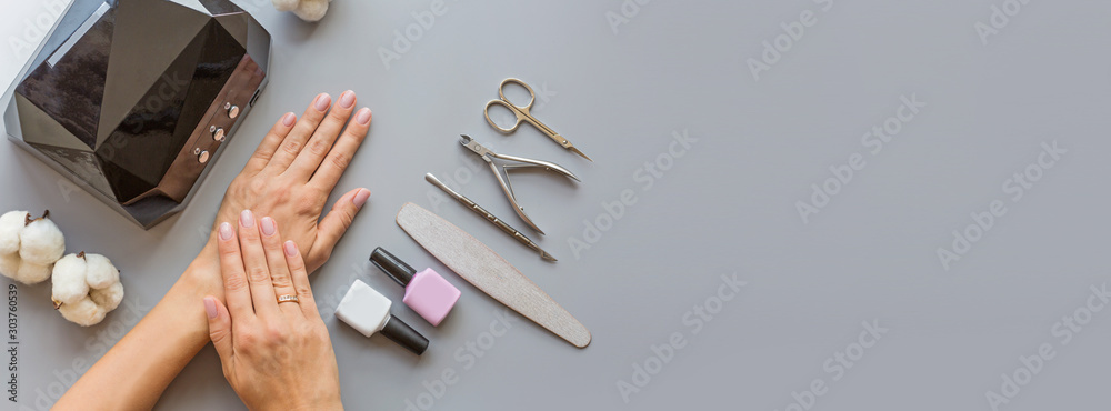 Stylish trendy manicure accessories with gel nail polishes, scissors, cuticle pusher, led lamp and flowers. Flat lay, top view, mock up, copy space template, overhead Stylish trendy manicure accessories with gel nail polishes, scissors, cuticle pusher, led lamp and flowers. Flat lay, top view, mock up, copy space template, overhead