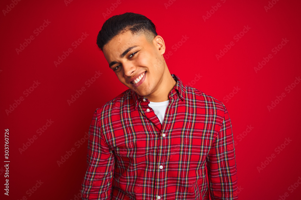 Young brazilian man wearing shirt standing over isolated red background looking away to side with smile on face, natural expression. Laughing confident. Young brazilian man wearing shirt standing over isolated red background looking away to side with smile on face, natural expression. Laughing confident.