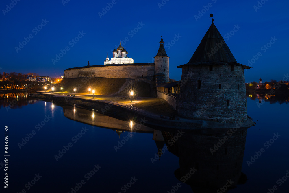 Night panorama of the city. Lanterns illuminate the walls and towers of the medieval fortress and are reflected in the water of the river. Pskov, Russia.