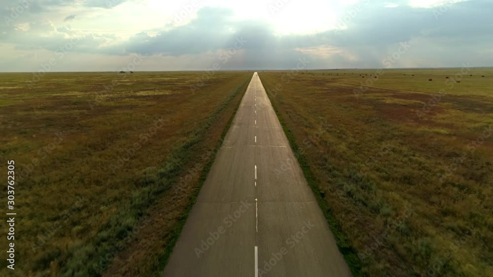 Lonely asphalt road highway rural track way route through natural landscape boundless steppe haystack agricultural field horizon. Dramatic sky clouds sunrise divine rays. Calm pacified. Aerial forward