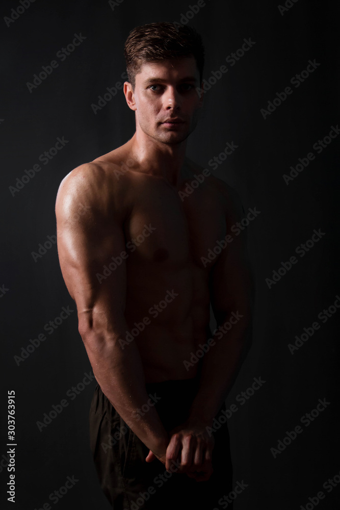 Muscular bodybuilder posing with a naked torso on a black background in the dark with backlight. Sexy man. Muscular bodybuilder posing with a naked torso on a black background in the dark with backlight. Sexy man.