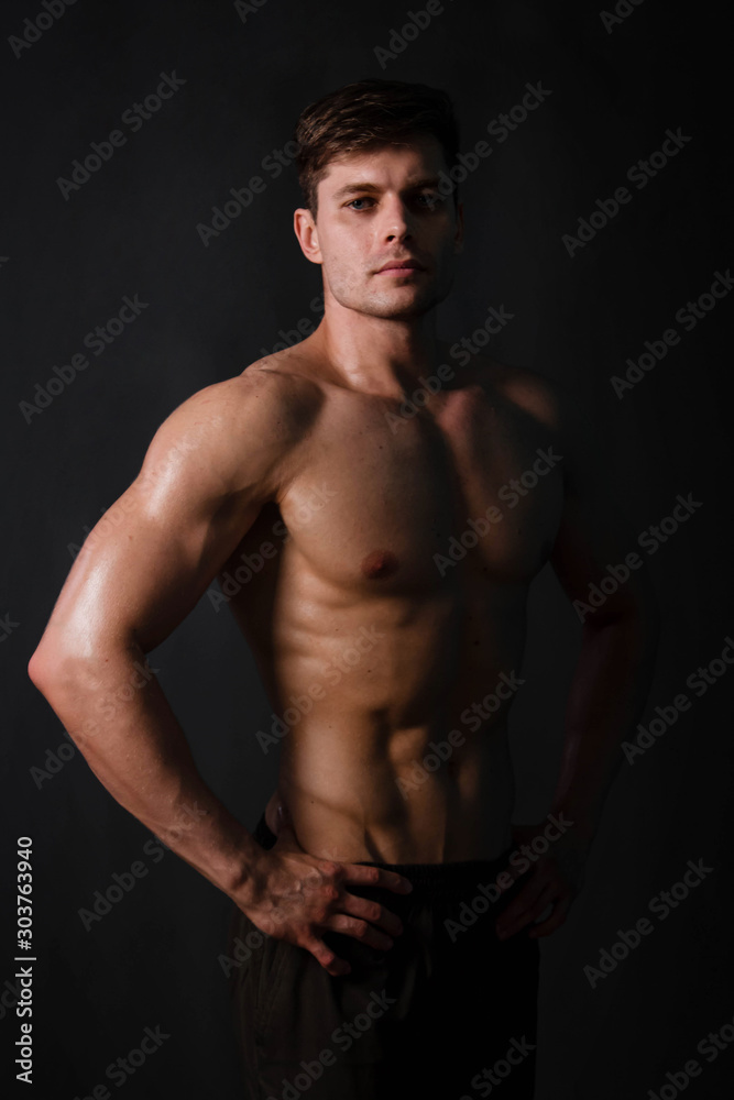 Muscular bodybuilder posing with a naked torso on a black background in the dark with backlight. Sexy man. Muscular bodybuilder posing with a naked torso on a black background in the dark with backlight. Sexy man.