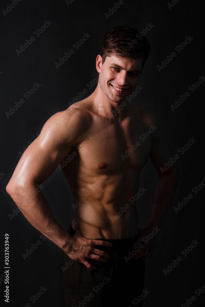 Muscular bodybuilder posing with a naked torso on a black background in the dark with backlight. Sexy man.