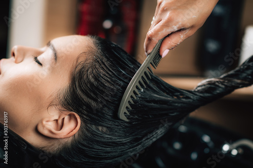 Hairdresser brushing woman’s long black hair.