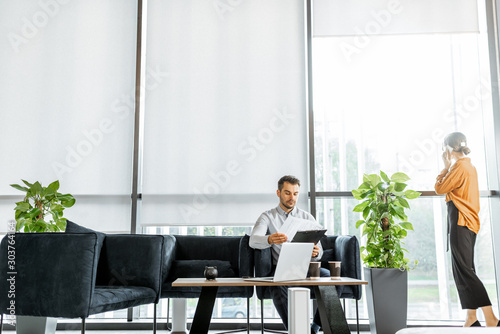 Young couple solving some business or legal affairs at the bank or financial institution office. Wide view with big window and copy space