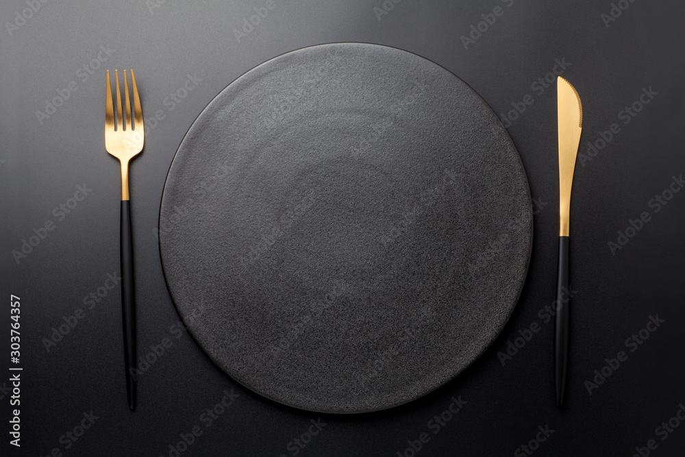 Empty black plate with fork and knife on black background. Top view. - obrazy, fototapety, plakaty 