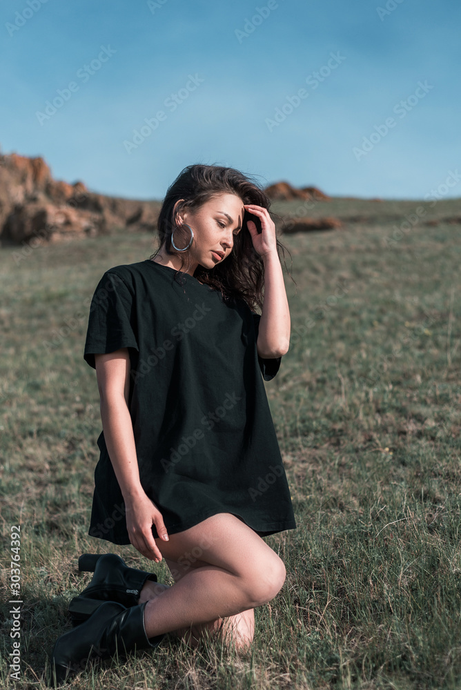 portrait of beautiful sexy brunette in black long t-shirt and black boots. fashionable woman in short dress outdoors in Sunny weather. men's t-shirt on woman