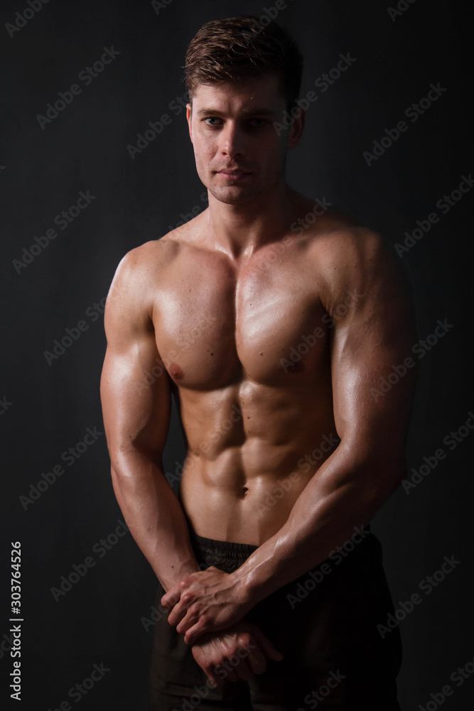 Muscular bodybuilder posing with a naked torso against a black background. Sexy man. Muscular bodybuilder posing with a naked torso against a black background. Sexy man.