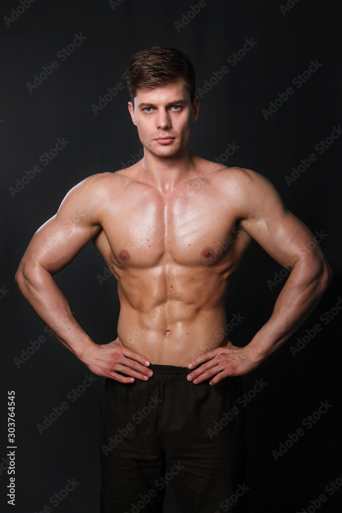 Naklejka premium Muscular bodybuilder posing with a naked torso against a black background. Sexy man.
