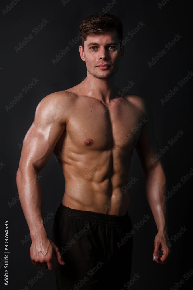 Muscular bodybuilder posing with a naked torso against a black background. Sexy man.