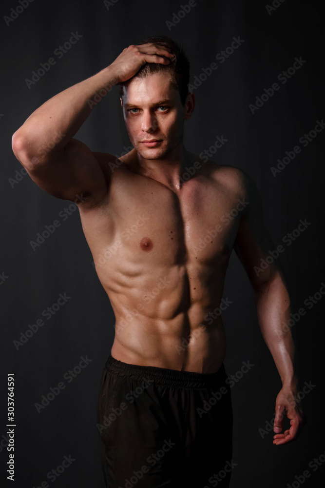 Muscular bodybuilder posing with a naked torso against a black background. Sexy man. Muscular bodybuilder posing with a naked torso against a black background. Sexy man.