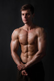 Muscular bodybuilder posing with a naked torso against a black background. Sexy man.