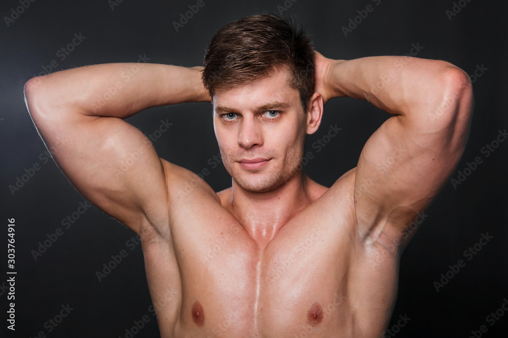 Bodybuilder holds muscular arms on head. Photo in studio on a black background. Bodybuilder holds muscular arms on head. Photo in studio on a black background.