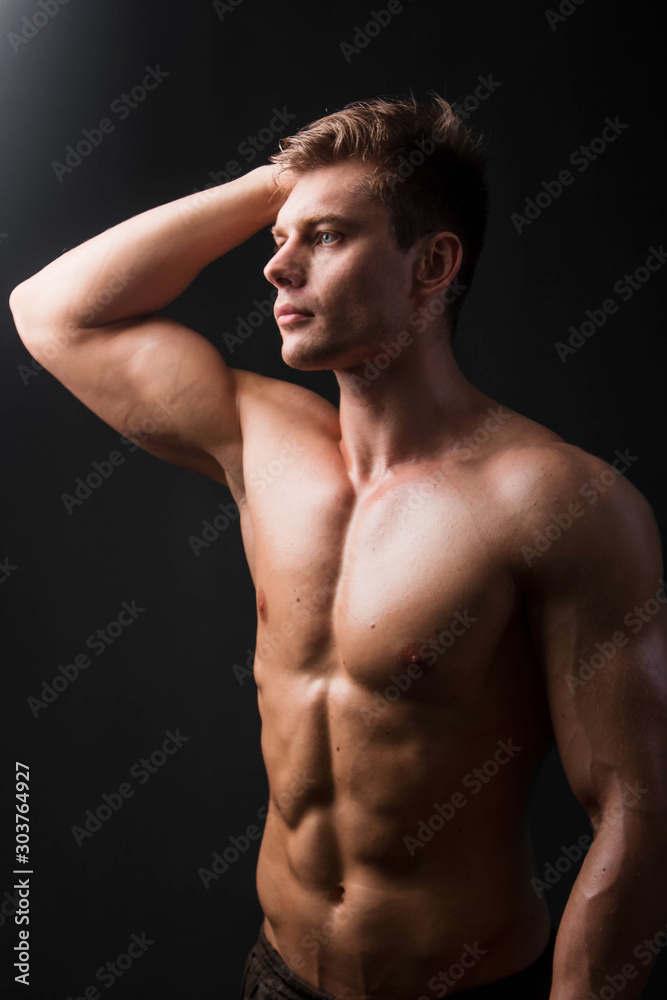 Bodybuilder holds muscular arms on head. Photo in studio on a black background.