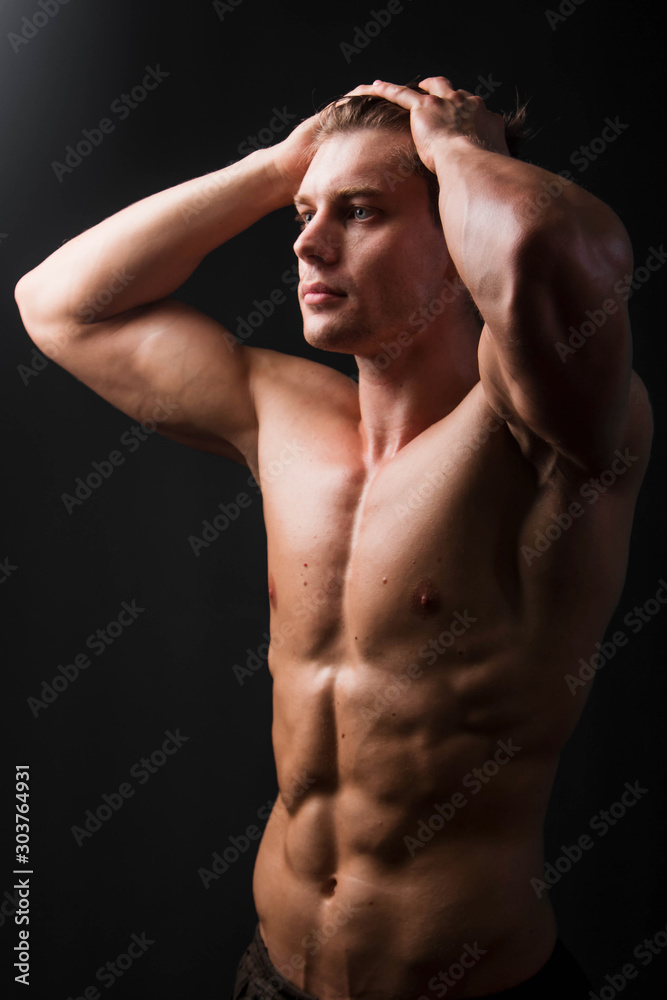 Bodybuilder holds muscular arms on head. Photo in studio on a black background.